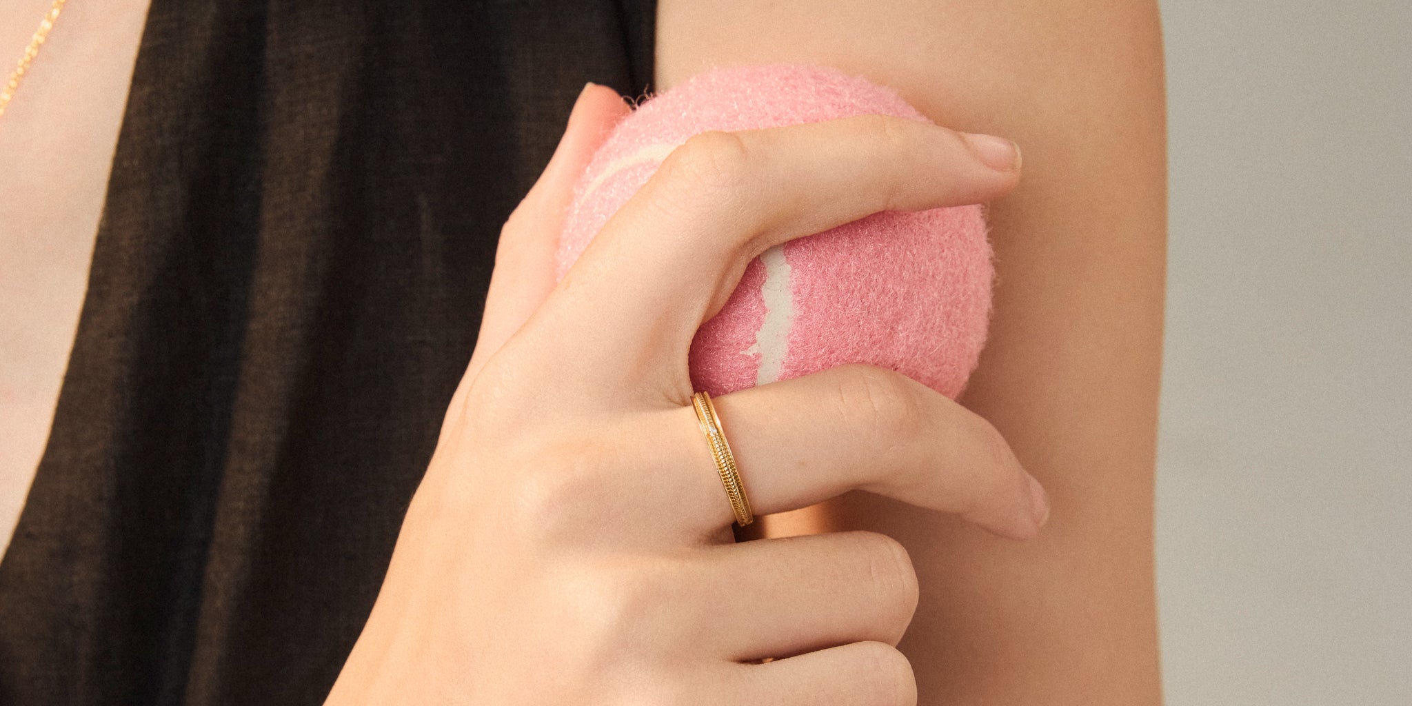 Hand holding a pink tennis ball against a neutral background with Stanza Thread Ring