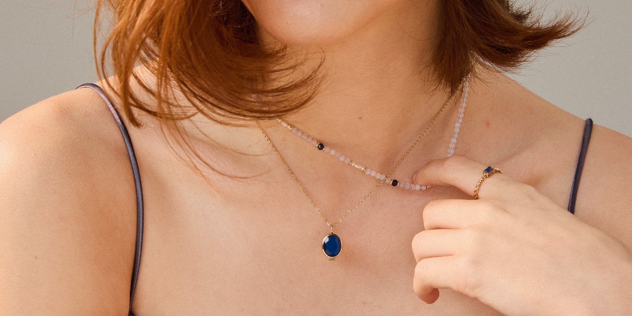 Person wearing a necklace with a blue pendant, holding it with their hand.